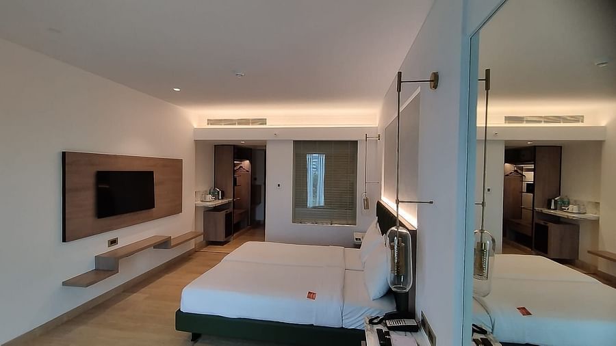 A modern executive room in Mirage Hotel, featuring twin beds with decorative head-rest, a large mirror, and a wooden panelled entertainment unit.