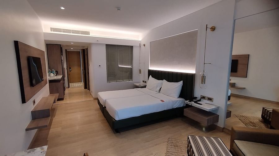A wooden floored executive bedroom in Mirage Hotel, featuring twin beds, a large mirror, lounge chairs, and an entertainment unit.