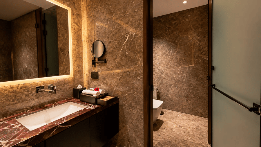 Loom room bathroom at Ni Central Park featuring a marble washbasin counter, LED mirror, and textured wall tiling.