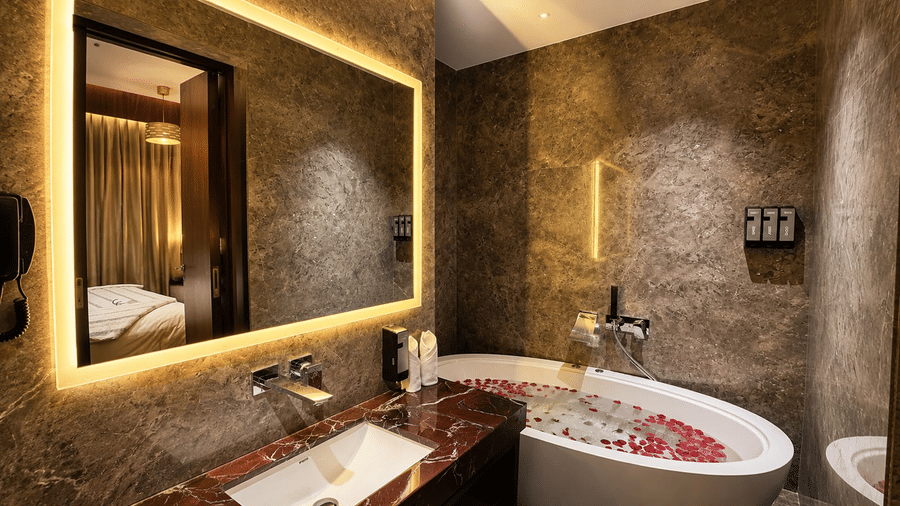 Zari bathroom featuring a freestanding soaking tub decorated with flower petals and a backlit vanity mirror.