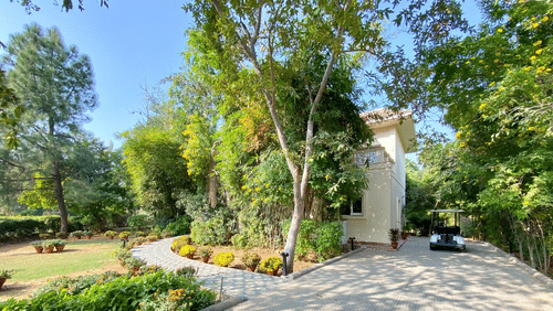 A huge house with green trees and lawn inside the compound, pictured with a golf cart parked on the front of the house - Karma Lakelands.