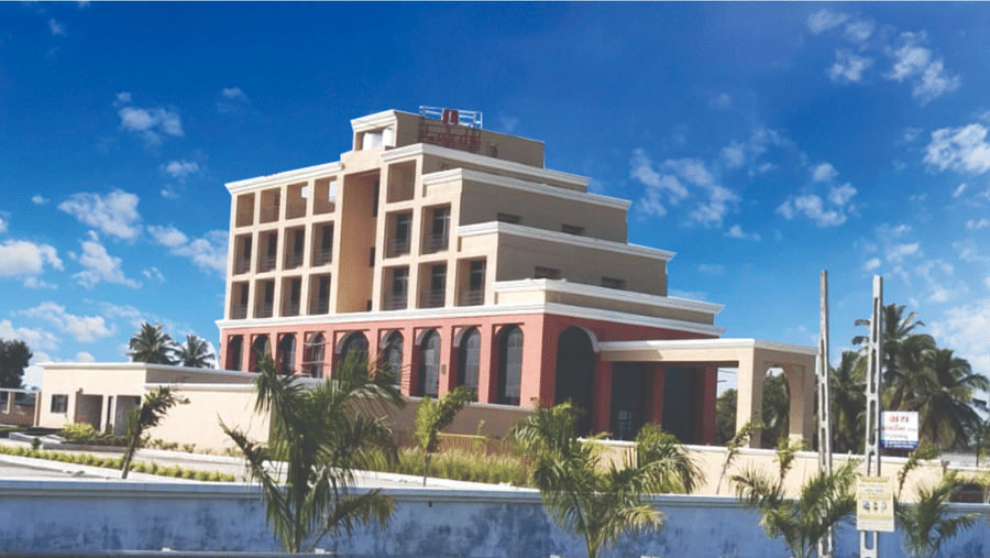Multi-storey modern hotel building exterior of Lords Swastik Studio, Kodinar, surrounded by plants under a bright sky.