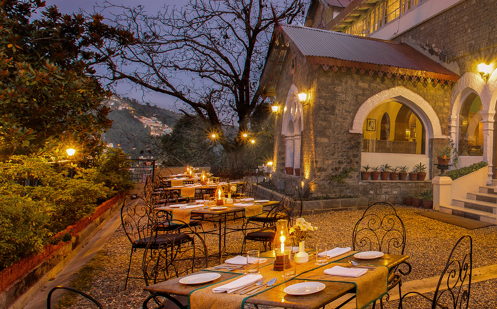 Pairs of tables places with chairs to accommodate up to 4 people on a set, in a outdoor setting in front of a house's entrance.