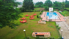 Full view of the Poolside Party Lawn featuring chairs and tables set on the lawn by the pool under a cloudy sky - VITS Kamats Resort, Silvassa