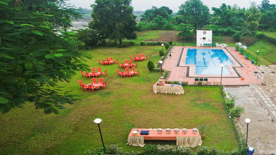 Full view of the Poolside Party Lawn featuring chairs and tables set on the lawn by the pool under a cloudy sky - VITS Kamats Resort, Silvassa