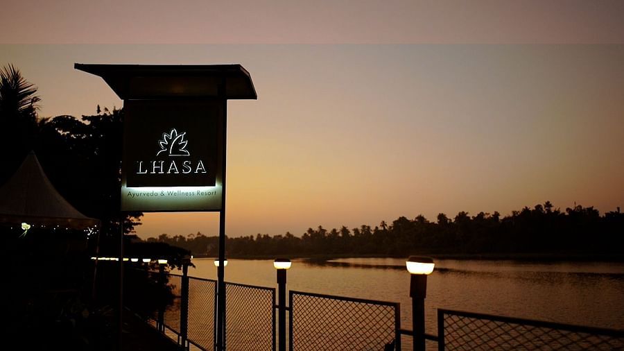 A sign with the word LEISURE stands illuminated by a lake at dusk, with warm sunset colors in the background.