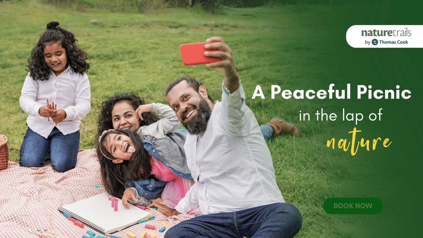 A creative banner which says A Peaceful Picnic in the Lap of Nature. It features a couple with their two daughters at Nature Trails Resort taking a selfie.