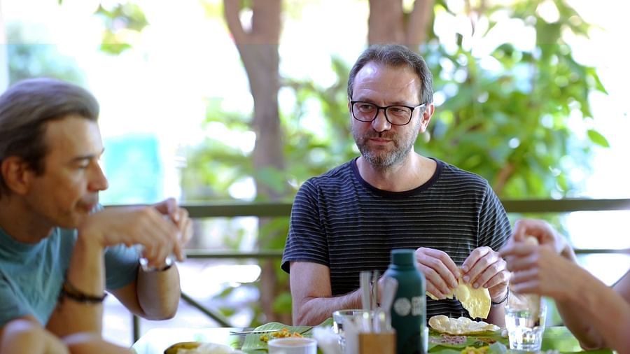 Three people are seated around a table outdoors, sharing a meal and conversation.