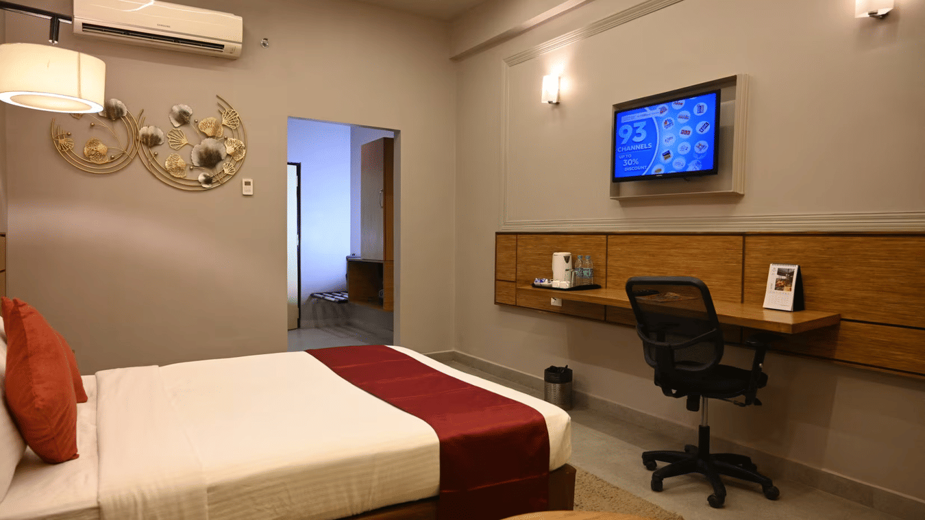 Modern hotel room with a comfortable bed, wall-mounted TV, and a work desk, featuring stylish decor and soft lighting at Max Hotel Prayagraj