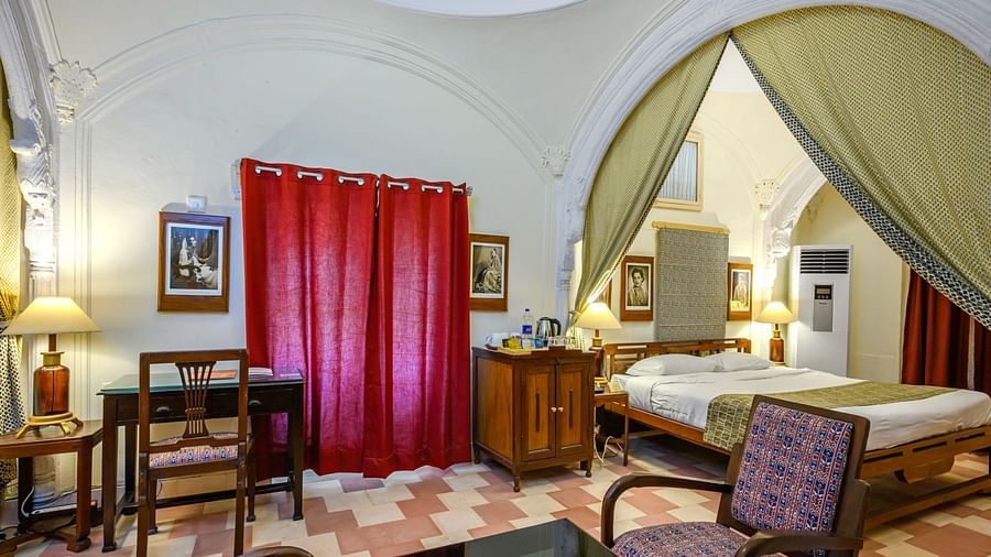 A room with a bed, a window, artwork on the wall, a fabric canopy, and a view into another room at Tijara Fort-Palace - 19th Century, Alwar.
