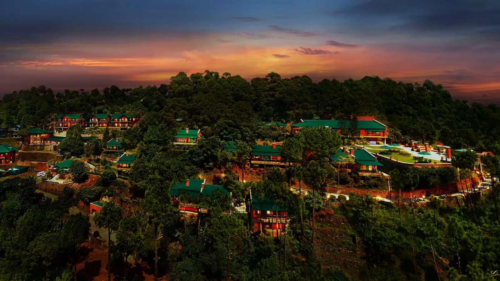 An aerial view of villas perched atop a mountain in the evening, with the sun setting behind them, casting a warm glow