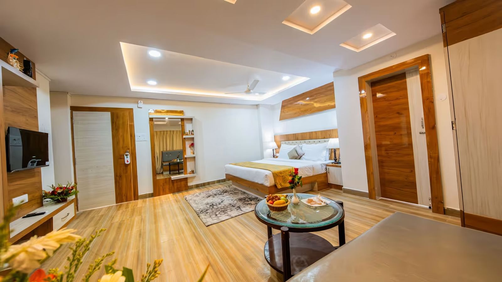 A spacious room with a large bed, wooden bedside tables on either side, and a wall-mounted television facing the bed.