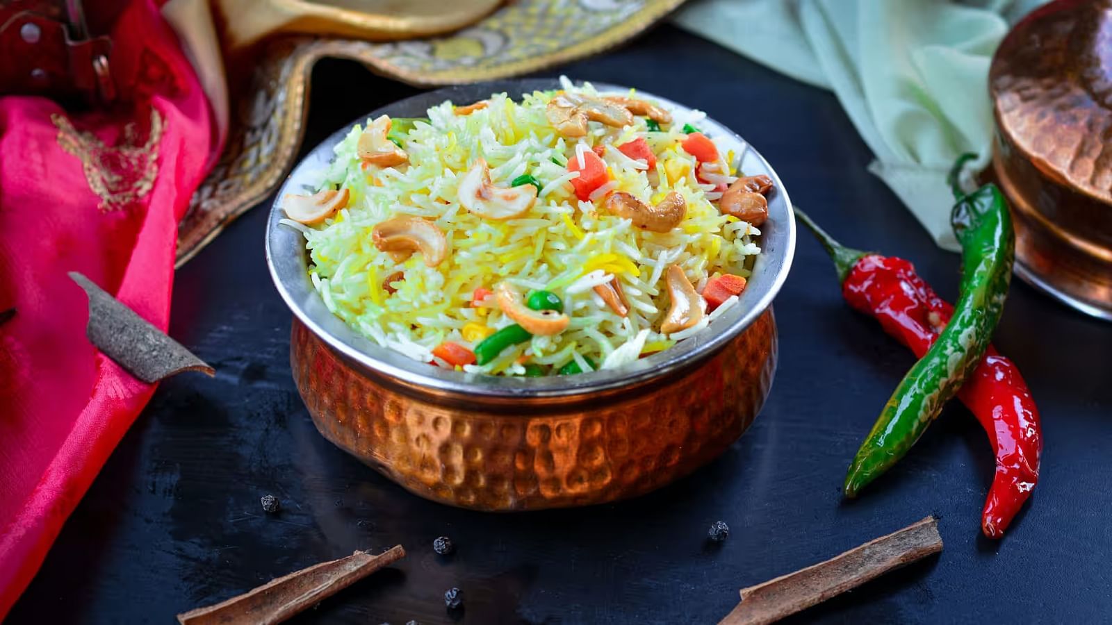 Chicken Biryani served in a traditional copper bowl, topped with vegetables and accompanied by a side of chillies.