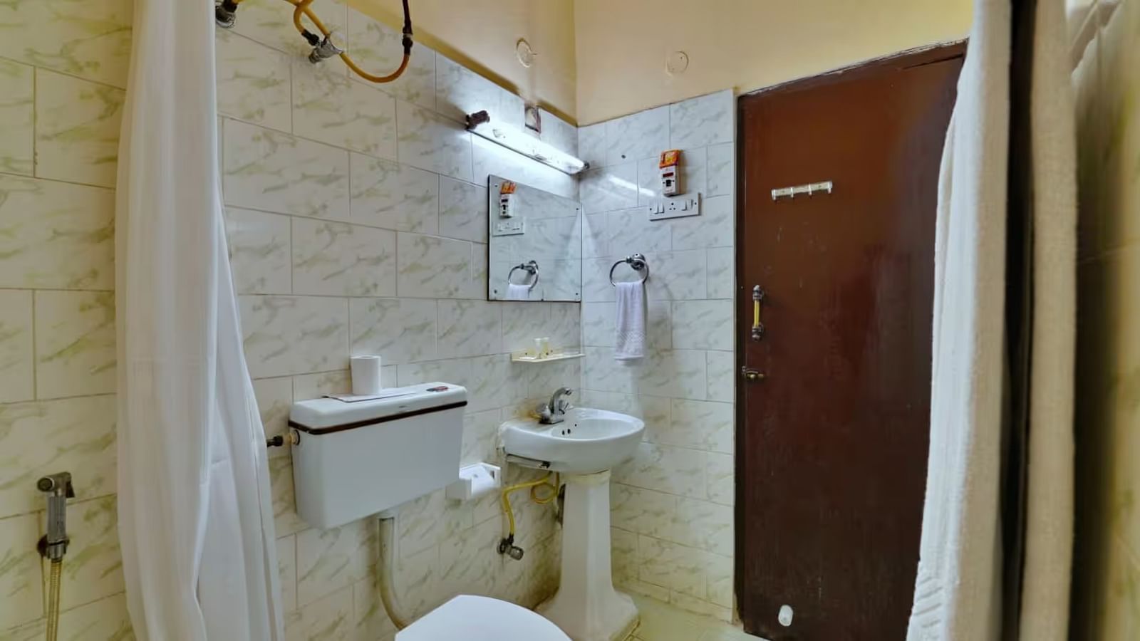  A bathroom with a western toilet, towels hung on a rack, a washbasin with toiletries on the side, and a mirror mounted directly above it.