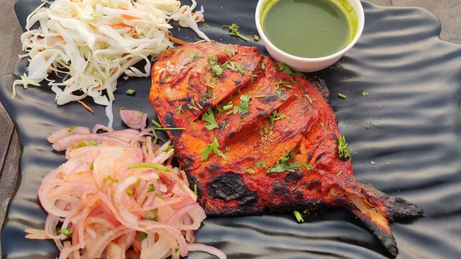Grilled pomfret served with onions on the side and a small bowl of green dipping sauce.