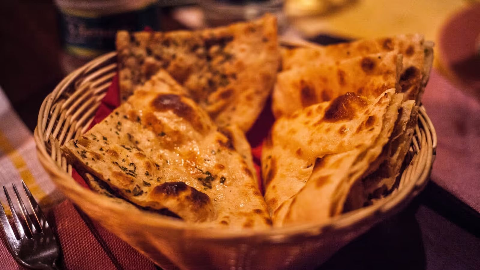  A wire basket filled with triangle-shaped roti, each brushed with ghee on the surface.