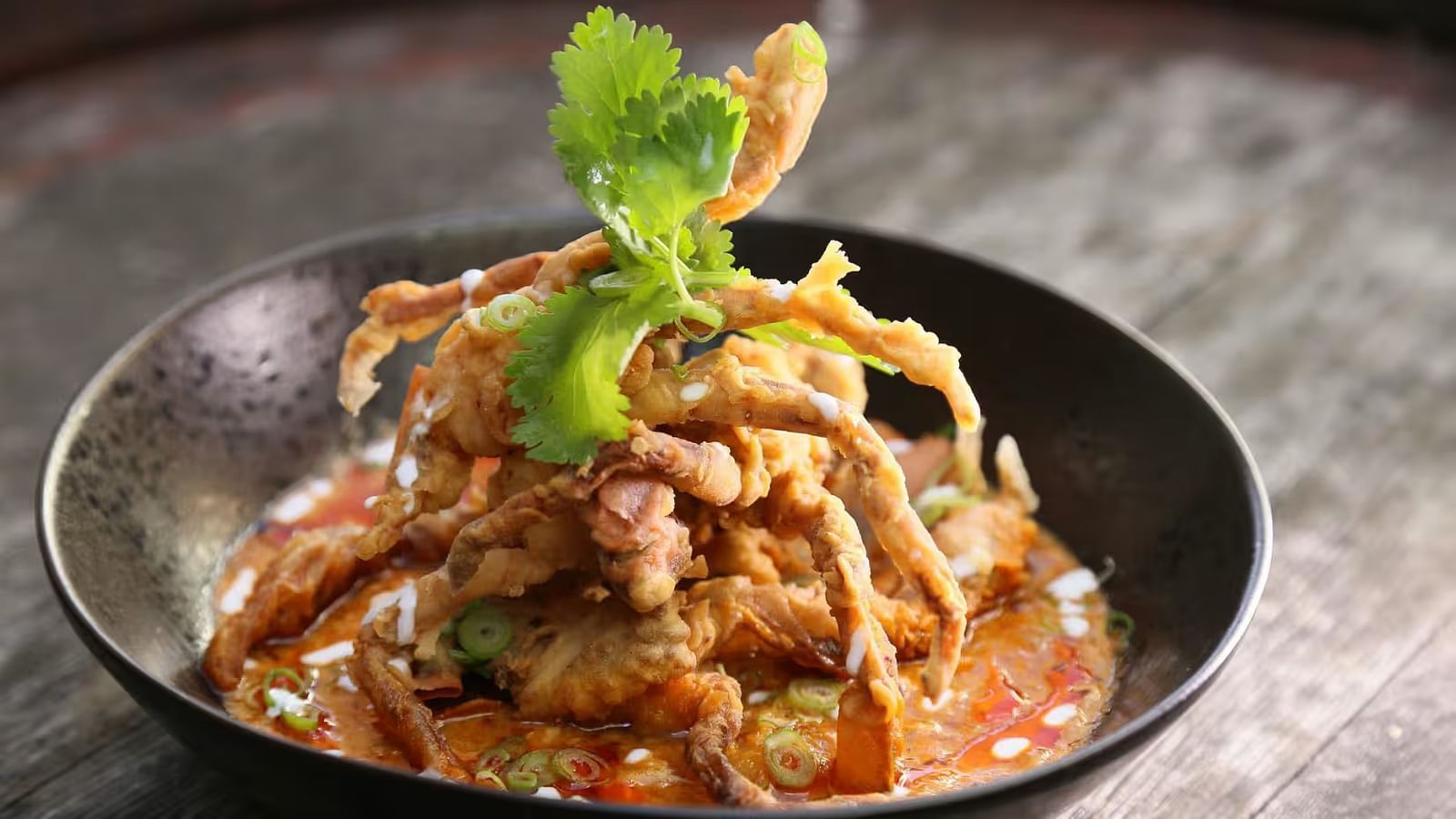 Soft shell crab curry in a bowl, garnished with curry leaves on top.