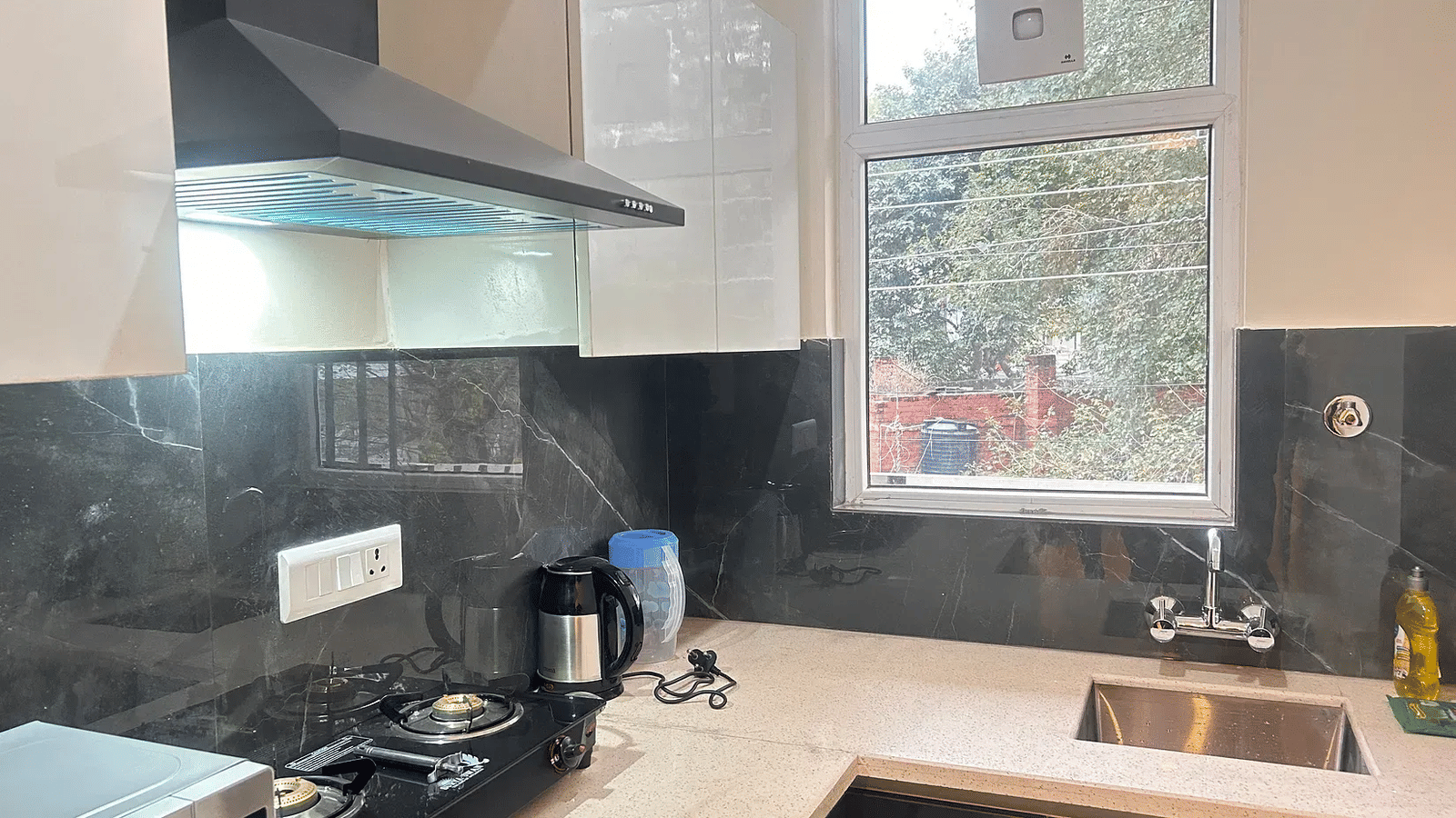 Modern kitchen countertop with cooking hob chimney sink and window ventilation at Lime Tree 1BHK Serviced Apartment Near Medanta Hospital Gurgaon for convenient residential stay