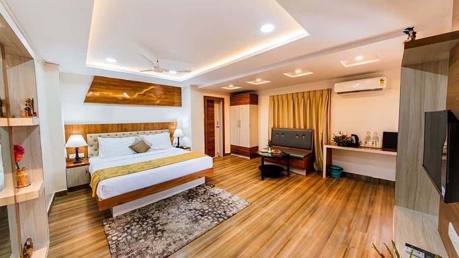  A spacious room with a bed and bedside table with lamps, a wall-mounted shelf adorned with decorative elements, and a sofa, table, and desk positioned on the opposite side.