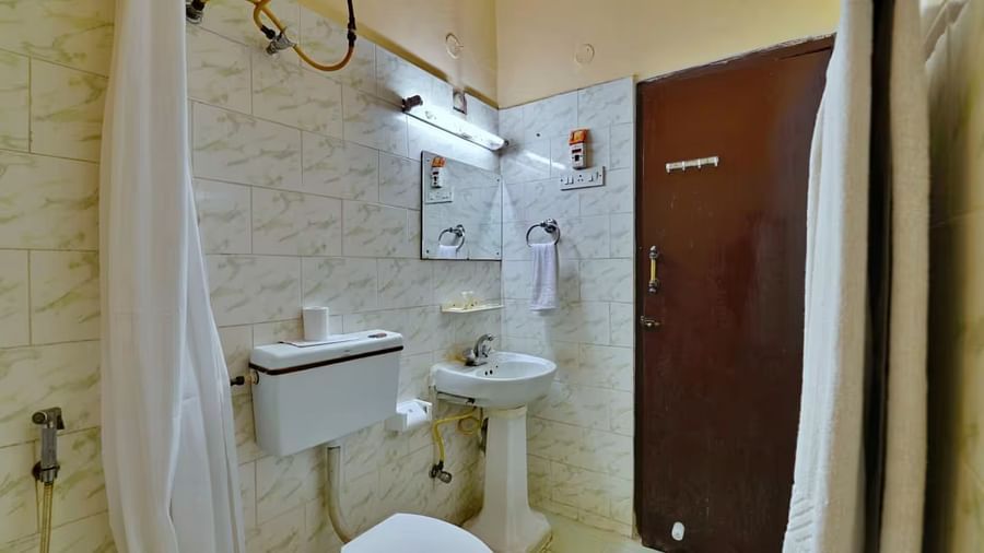  A bathroom with a western toilet, towels hung on a rack, a washbasin with toiletries on the side, and a mirror mounted directly above it.