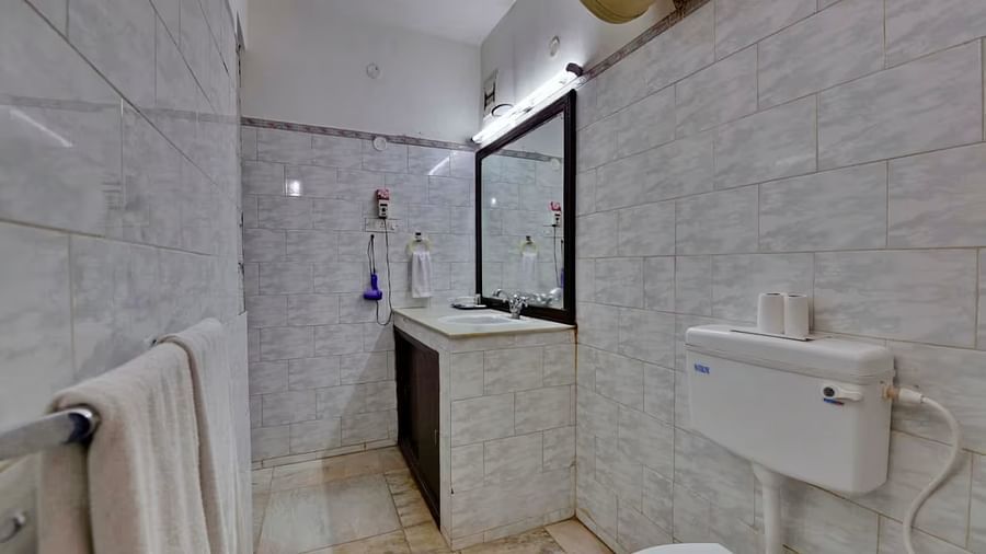 A bathroom with a western toilet, towels hung on a rack, a washbasin with toiletries on the side, and a mirror mounted directly above it.