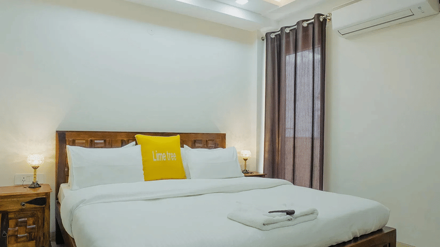 Double bed with a carved wooden headboard, a yellow cushion and bedside lamps at Lime Tree Hotels, Golf Course Extension Road