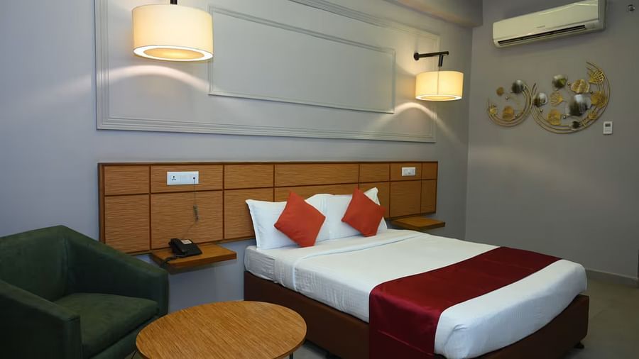 View of an elegant hotel room with a king size bed, warm lighting, and a cosy seating - Max Hotel Prayagraj.