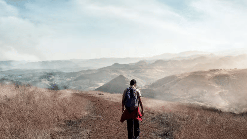 A person in dark clothing standing on rocky terrain with barren hills in the background.