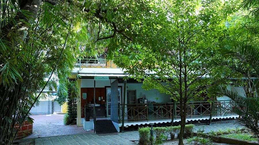 A building with glass doors and a patio is partially obscured by lush green trees.