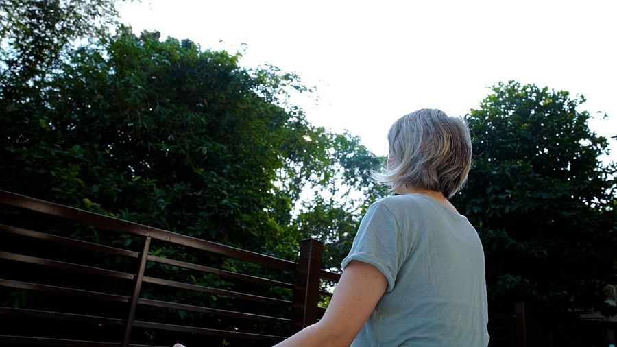 A person sits in a yoga pose outdoors, with their back to the viewer and greenery in the background.