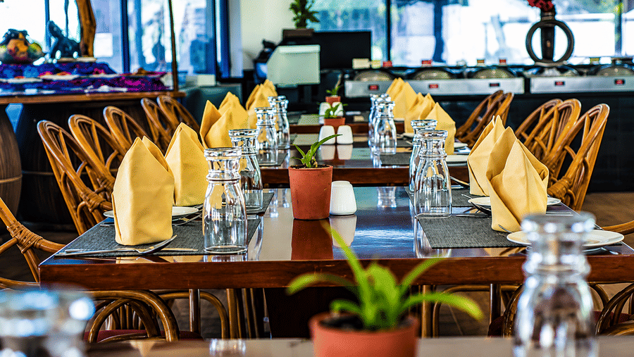 Kapi Multicuisine Restaurant table set with yellow napkins, glassware, and wicker chairs, offering an elegant dining experience