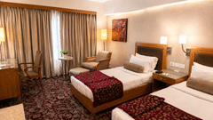 Twin beds with patterned carpet, lamps, and cozy seating area at Pride Plaza Ahmedabad.