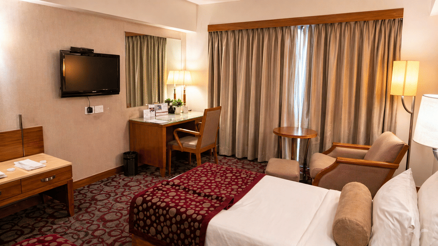 Twin room with TV, work desk, cushioned chair, and curtained window at Pride Plaza Ahmedabad.