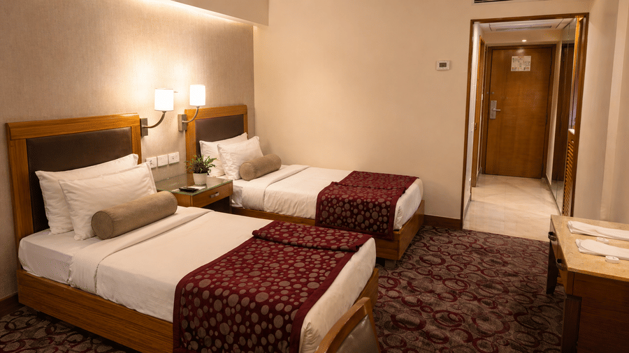 Twin beds with white linens, bedside lamps, and patterned carpet at Pride Plaza Ahmedabad.
