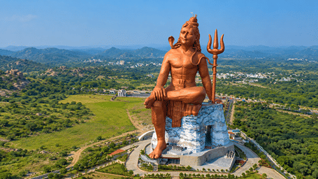 Aerial view of the massive copper-coloured Statue of Belief (Vishwas Swaroopam) depicting Lord Shiva seated amidst lush green hills.