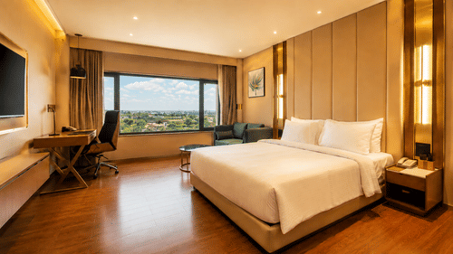 A room includes a king size bed, a wooden desk with an office chair, and a wall mounted television at Pride Plaza Indore.