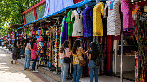 A shopping street showcasing several people standing near the shops with clothes hung outside.