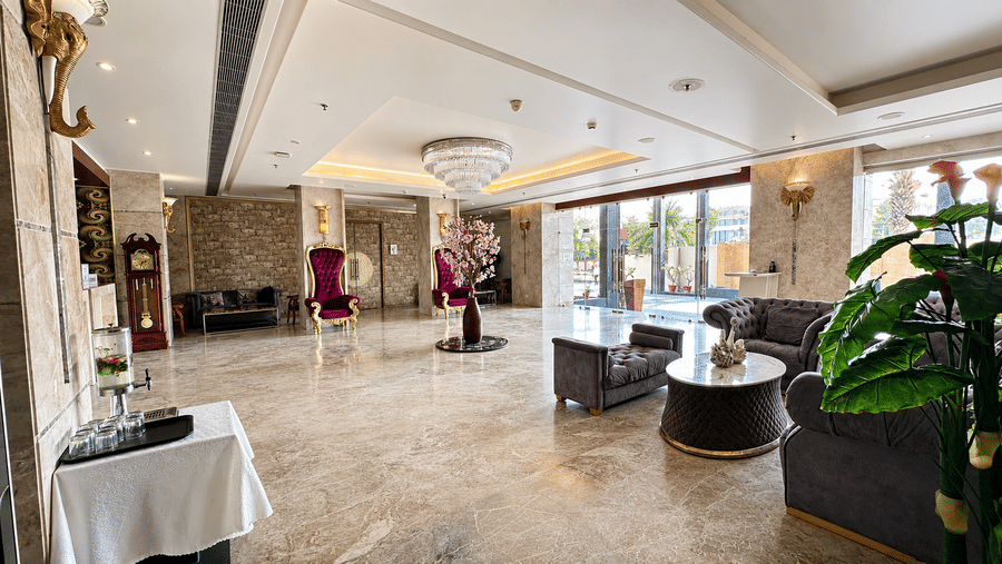 Spacious hotel lobby at Golden Tulip Kukas Jaipur with marble floors, dining setup on the left, indoor plants, and large windows allowing natural light.