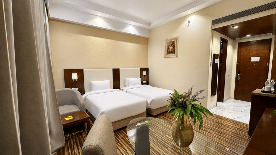 Superior Twin room at Golden Tulip Kukas Jaipur with two single beds, white bedding, striped carpet flooring, beige walls, and a decorative plant by the window