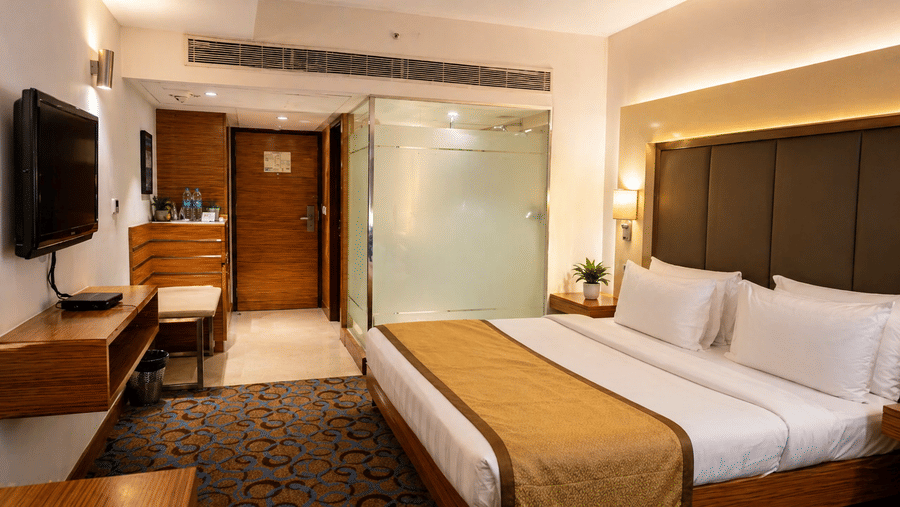 Neat room with a single bed, wooden desk, TV, and soft lighting at Pride Plaza Ahmedabad.