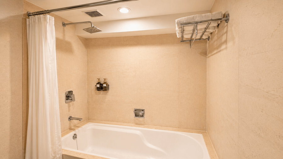 Bathtub with shower curtain, wall fixtures, and overhead rack in a clean bathroom at Pride Plaza Ahmedabad.