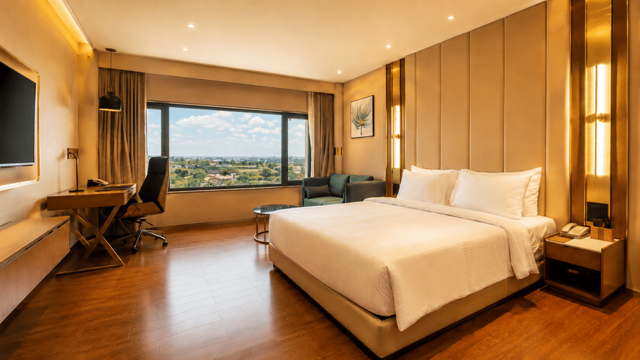 A room includes a king size bed, a wooden desk with an office chair, and a wall mounted television at Pride Plaza Indore.