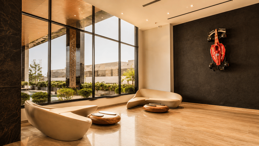 Curved cream sofas stand near round wooden tables, a large window panel, and a wall sculpture on a polished floor at Pride Plaza Indore.