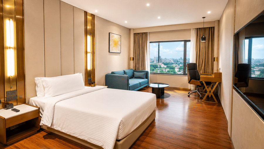 Superior King Room at Pride Plaza Indore featuring a bed, bedside table, sofa, coffee table, work desk with chair, and a window with a city view.