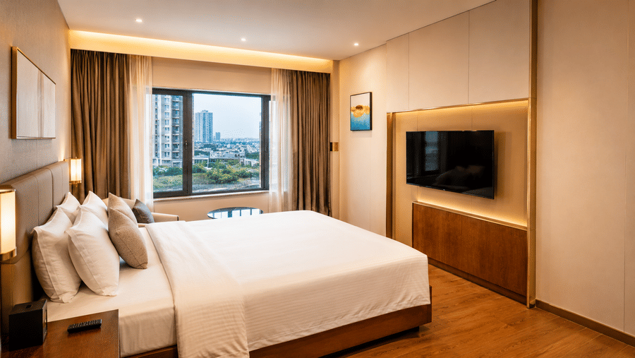 Superior King Room at Pride Plaza Indore featuring a king bed, bedside tables, a wall-mounted television on a panel, and a window with drapery.