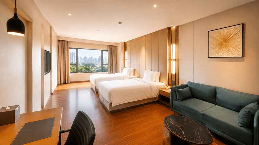 Superior Twin Room at Pride Plaza Indore showing 2 single beds, a large window, a sofa with a coffee table, and a desk with a chair.