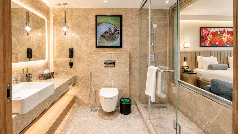 Modern bathroom at Pride Premier Pune with a vanity, toilet, glass shower enclosure and marble finishes.