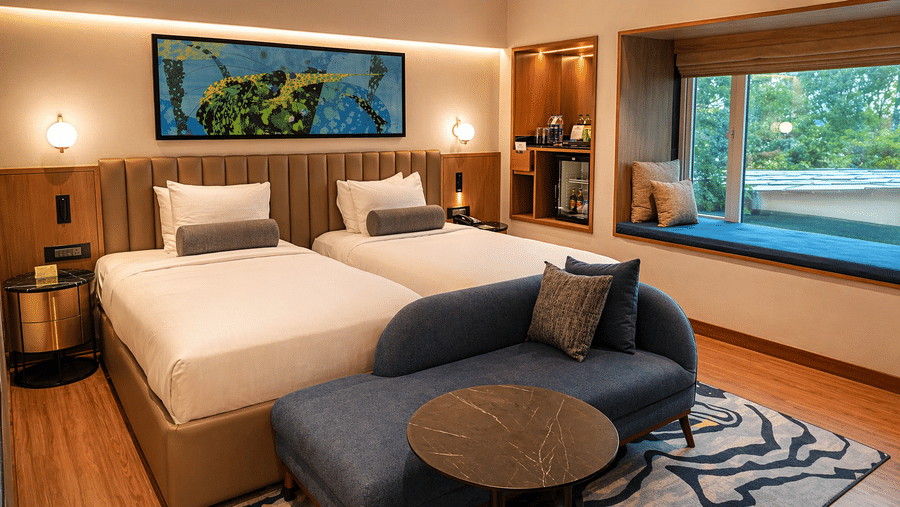 Guest room at Pride Premier Pune featuring a twin beds, lounge seating and a large window overlooking greenery.