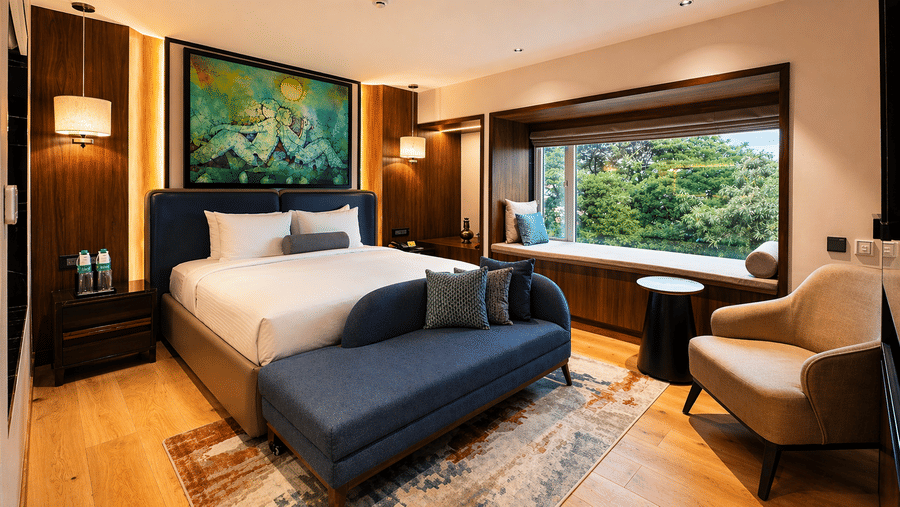 Guest room at Pride Premier Pune featuring a king size bed, seating area and large window overlooking greenery.