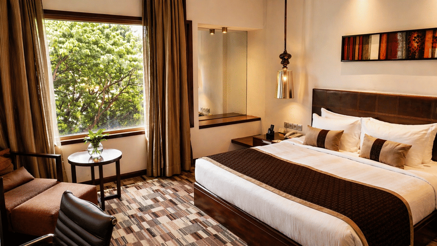 Bedroom at Pride Premier Pune with a king size bed, armchair, window seating and views of greenery.